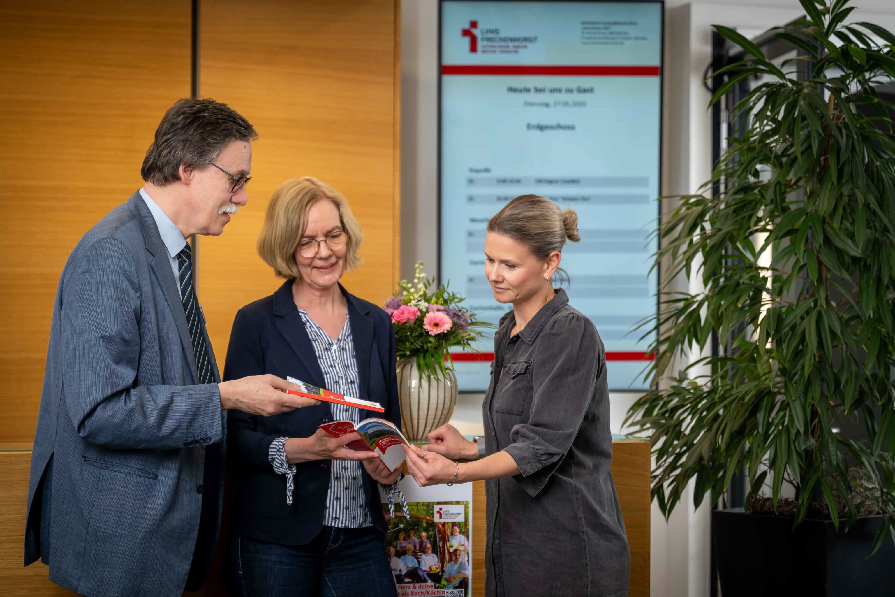 drei Personen die sich das Jahresprogramm 2025 angucken